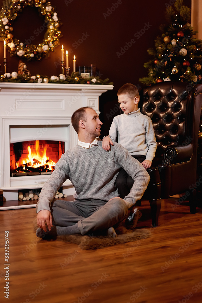 Father and son sitting on floor near the fireplace and the Christmas tree