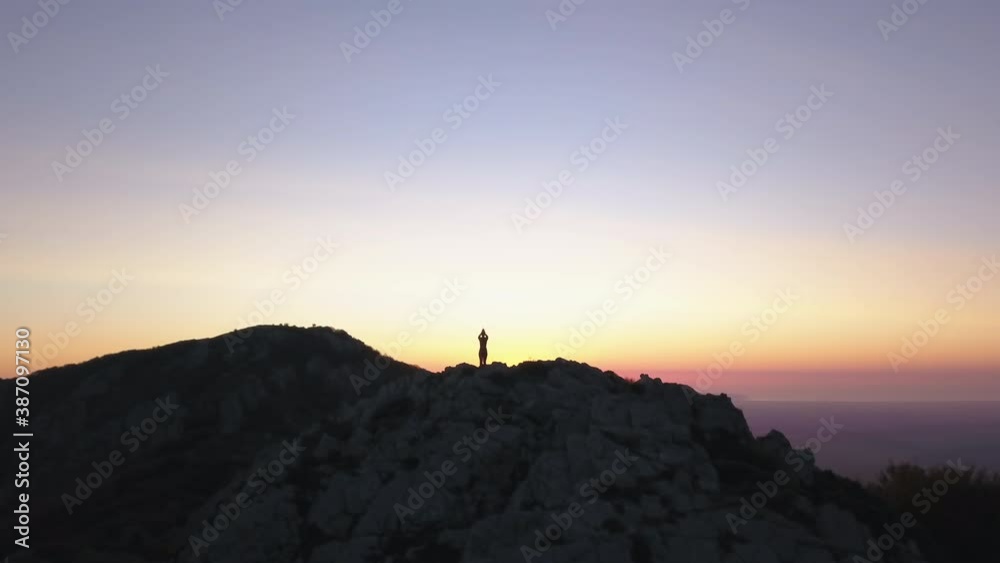 Smooth orbital drone shot of a woman doing yoga on top of a mountain. The sun rise behind the mountain. 4K Pro Res Smooth orbital drone shot of a woman doing yoga on top of a mountain. The sun rise behind the mountain. 4K Pro Res