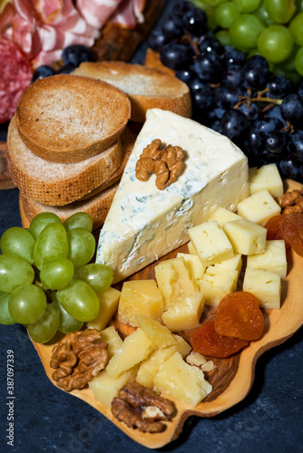 cheese platter on a wooden board, bread, fruit and cold cuts, vertical closeup