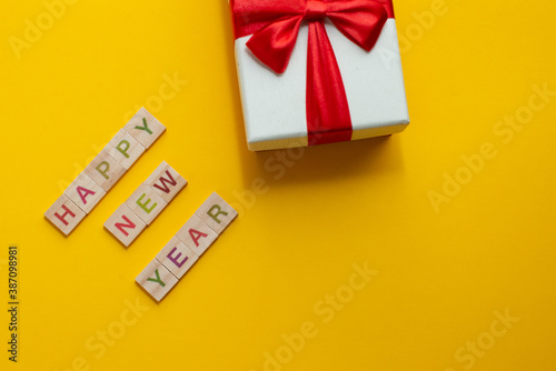 Happy New Year and Merry Christmas. Scrabble letters with holiday present on yellow background. Letter tiles spelling celebration holiday.