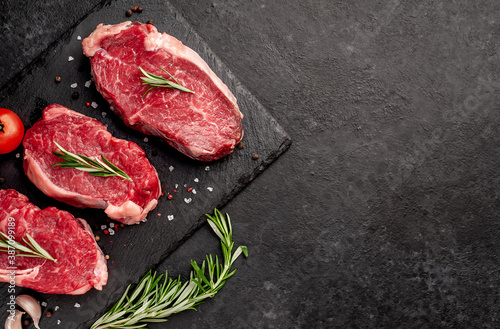  raw three beef steaks on a cutting board with spices on a stone background with copy space for your text