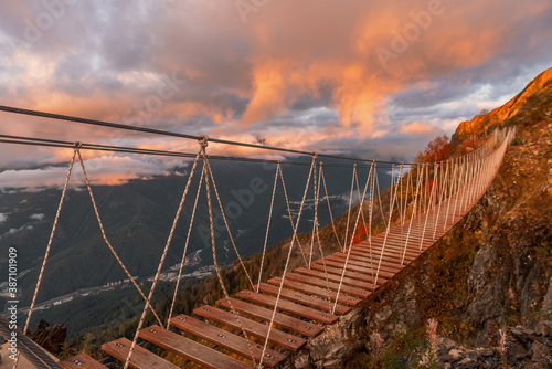 Suspension bridge in the mountains. Golden autumn in the light of the setting sun.