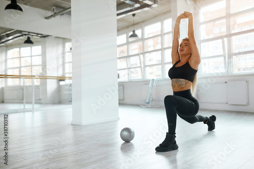 A pretty fit young woman doing frontal lunges or squats indoors. The blonde is engaged in the morning at dawn in the white room. Healthy lifestyle