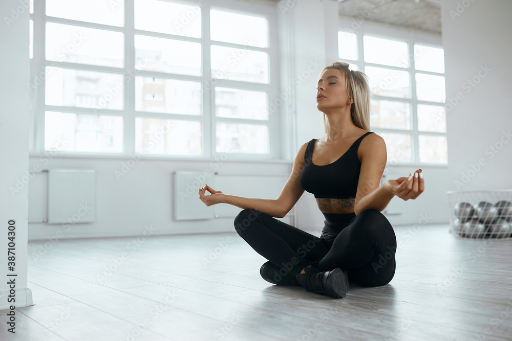 Yoga concept. The sportswoman sits in the lotus position in a light room on the floor. blonde in black suit