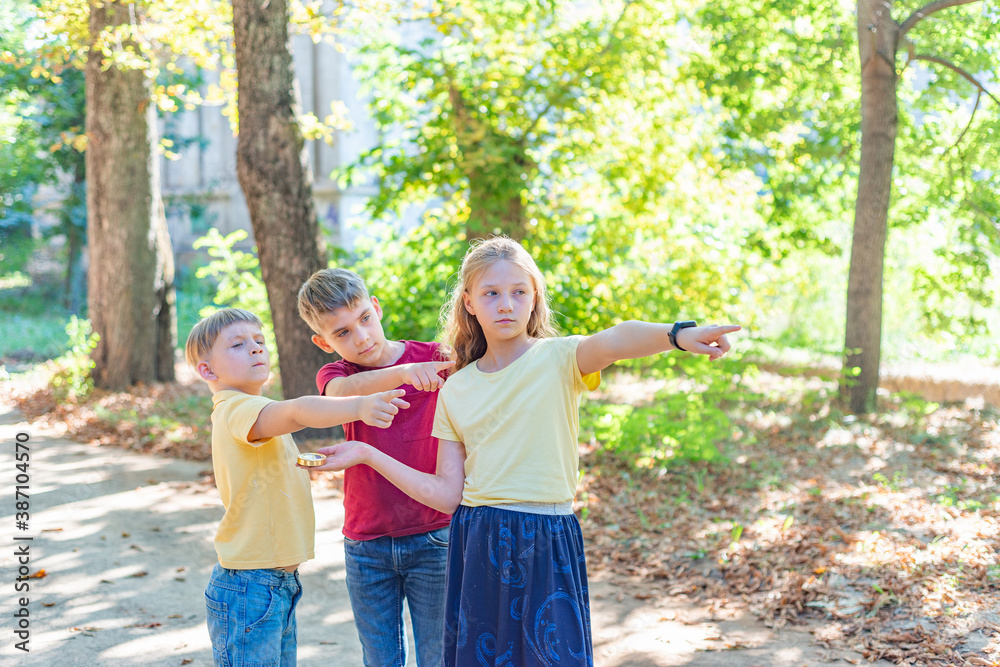 Fototapeta premium Children with a compass point their fingers where to go. Children's rest and entertainment in the park.