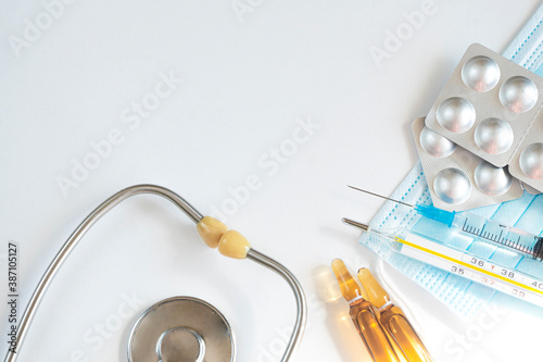 Syringe with vaccine, ampoules and various pills, thermometer, phonendoscope and medical equipment. Seasonal illness concept. Copy space. White background, top view photo