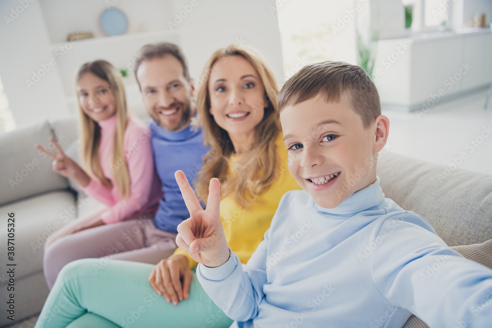 Photo of positive family people sit cozy couch mommy daddy take selfie two kids make v-sign in house indoors Photo of positive family people sit cozy couch mommy daddy take selfie two kids make v-sign in house indoors
