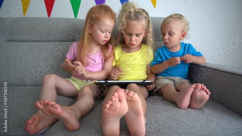 Friendly kids share one tablet computer sitting on sofa. Siblings with tablet pc