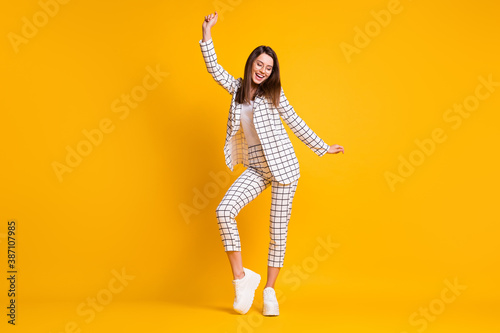 Full length body size photo of dancing girl wearing white checkered formal wear smiling isolated on bright yellow color background