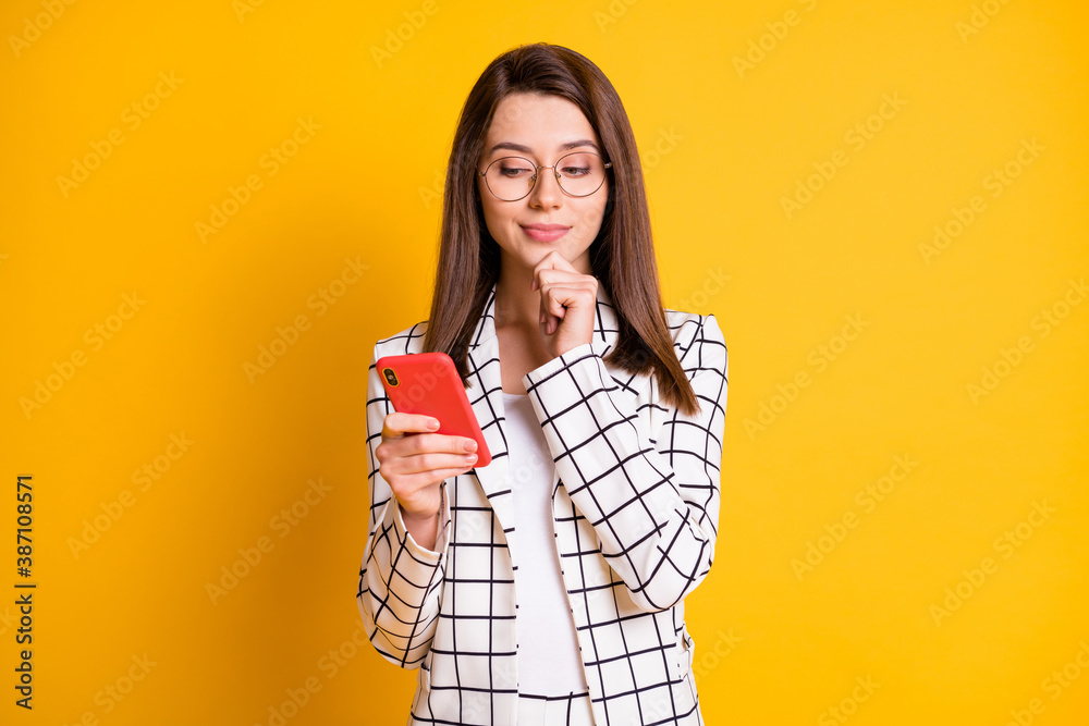 Photo portrait of curious businesswoman using smartphone touching face wearing spectacles isolated on vivid yellow color background Photo portrait of curious businesswoman using smartphone touching face wearing spectacles isolated on vivid yellow color background
