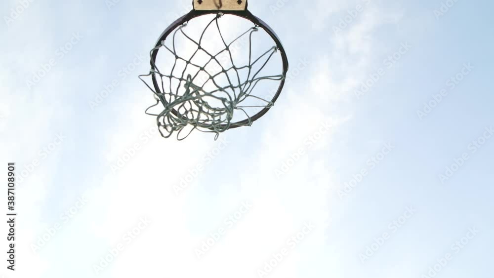 Bottom view of a basketball basket into which the ball flies. Hoop against the blue sky. Close up. Slow motion. Bottom view of a basketball basket into which the ball flies. Hoop against the blue sky. Close up. Slow motion.