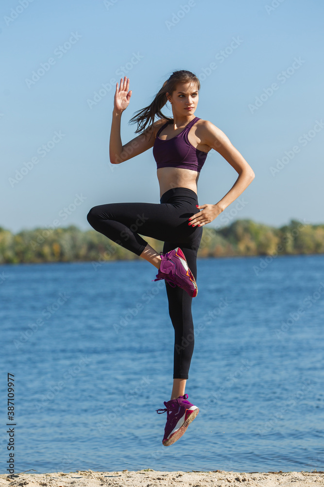Fototapeta premium High jump. Young female athlete, woman training, practicing outdoors in autumn sunshine. Beautiful caucasian sportswoman working out open-air. Concept of sport, healthy lifestyle, movement, activity.