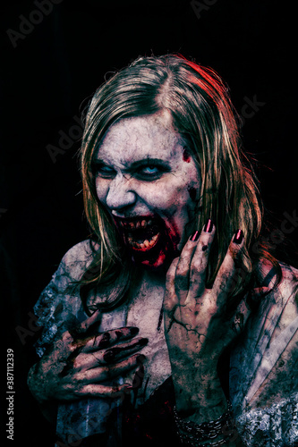 Studio portrait of a female vampire of zombie looking at camera. Black background.