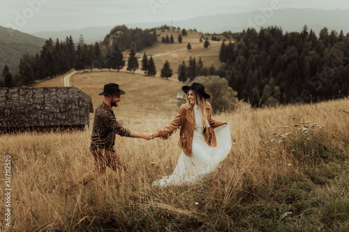 Beautiful stylish  couple walks holding hands in a Carpathian mountain landscape.