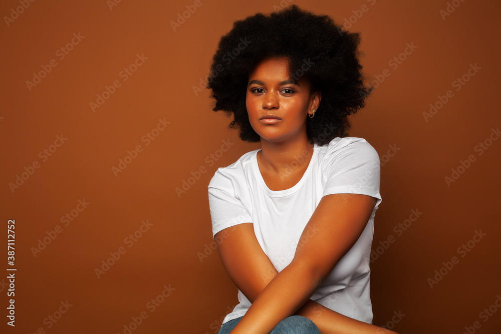 pretty young african american woman with curly hair posing cheerful gesturing on brown background, lifestyle people concept pretty young african american woman with curly hair posing cheerful gesturing on brown background, lifestyle people concept