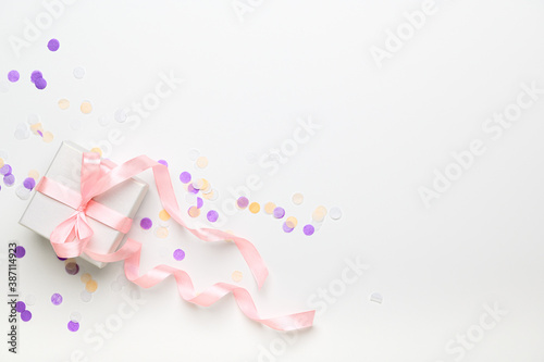 White box wrapped in pink ribbon on a white background top view. Gift for a holiday, christmas, birthday, women's day in pastel colors. Festive decor with confetti and present flat lay. Copy space