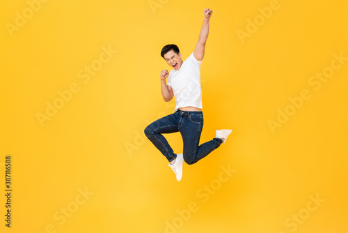 Young energetic Asian man  jumping and raising his fist isolated on yellow color background photo