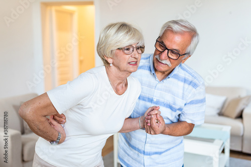 Senior couple at home. Handsome old woman is having back pain and her attractive old husband supports her.