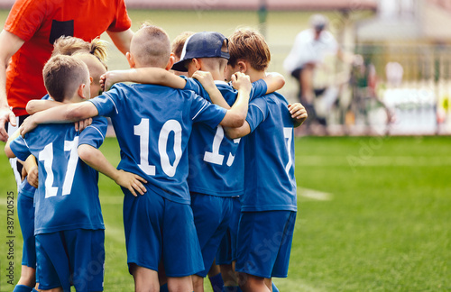 Kids in elementary school sports team with coach. Boys in blue soccer uniforms with white numbers on back. Coach motivate children football players before the game. School sports tournament for youth