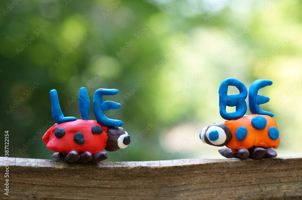 The inscription love in German. Next to it are two figures of ladybirds made of plasticine. The inscription love in German. Next to it are two figures of ladybirds made of plasticine.