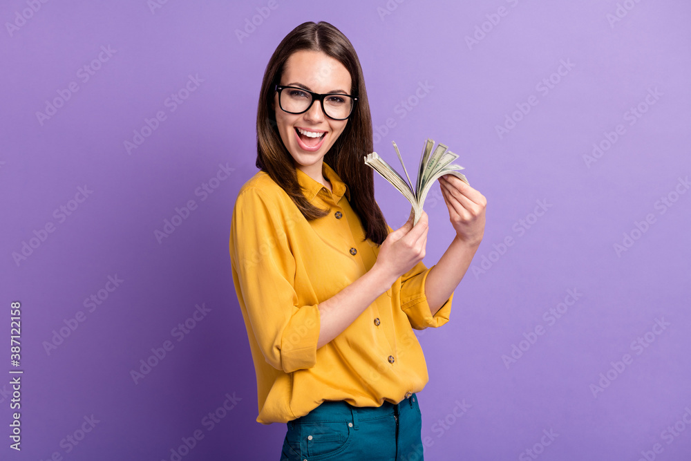 Photo of pretty young girl look camera hold pile cash open mouth wear spectacles yellow shirt isolated purple color background Photo of pretty young girl look camera hold pile cash open mouth wear spectacles yellow shirt isolated purple color background