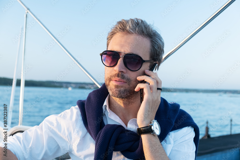 Handsome successful man on the yacht talking on mobile phone. Portrait of business man on sailing boat at sunset.