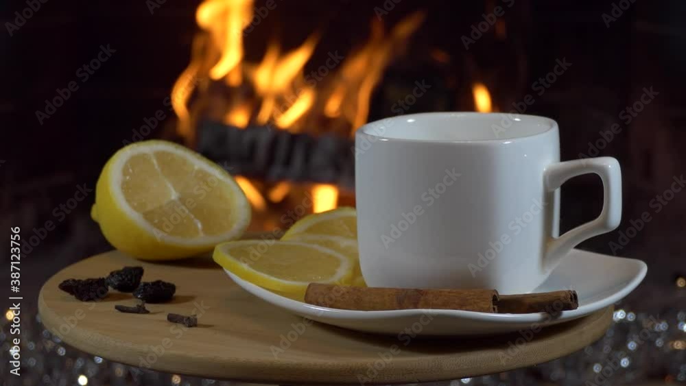 Christmas, New year, fireplace. One teacup, lemon, spices for mulled wine, festive decorations on the table against the background of the flame. Close up. Christmas, New year, fireplace. One teacup, lemon, spices for mulled wine, festive decorations on the table against the background of the flame. Close up.
