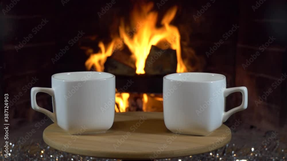 Christmas, New year, fireplace. Two empty tea cups stand on a small table against a background of flames and Christmas decorations. Close up. Christmas, New year, fireplace. Two empty tea cups stand on a small table against a background of flames and Christmas decorations. Close up.