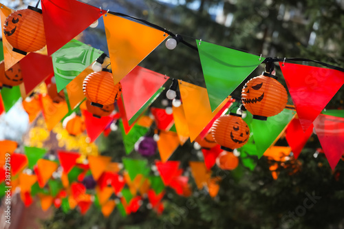 Colorful bunting paper cut  orange pumpkin lamps. Jack-o-lanterns hanging outdoors. Halloween street decoration  autumn holiday concept