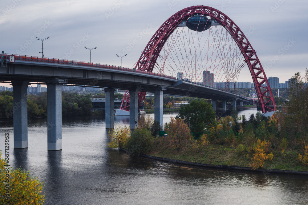 Scenic view of the Zhivopisny bridge in Moscow, Russian Federation. Photo shoot of red arch, steel cable-stayed bridge across the Moskva River. Cloudy autumn day. Side view. Scenic view of the Zhivopisny bridge in Moscow, Russian Federation. Photo shoot of red arch, steel cable-stayed bridge across the Moskva River. Cloudy autumn day. Side view.