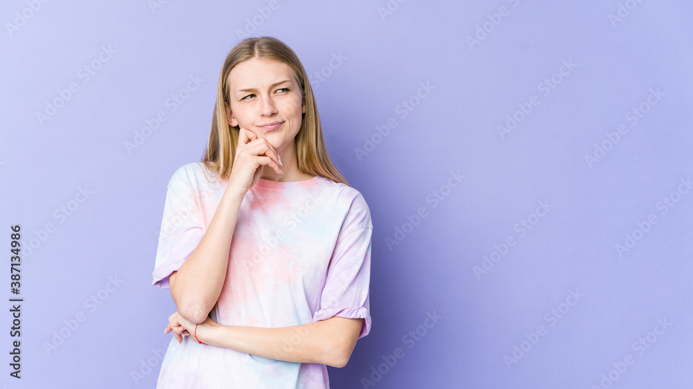 Young blonde woman isolated on purple background relaxed thinking about something looking at a copy space. Young blonde woman isolated on purple background relaxed thinking about something looking at a copy space.