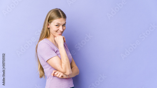 Young blonde woman isolated on purple background smiling happy and confident, touching chin with hand.