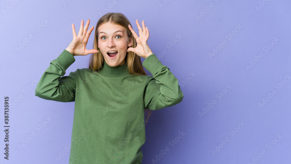 Young blonde woman isolated on purple background receiving a pleasant surprise, excited and raising hands. Young blonde woman isolated on purple background receiving a pleasant surprise, excited and raising hands.