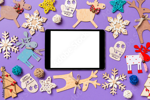 Festive decorations and toys on purple background. Top view of digital tablet. Merry Christmas concept