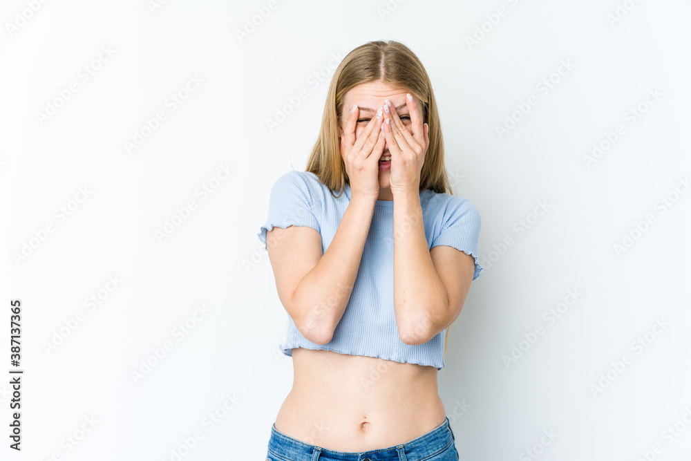 Fototapeta premium Young blonde woman isolated on white background blink at the camera through fingers, embarrassed covering face.