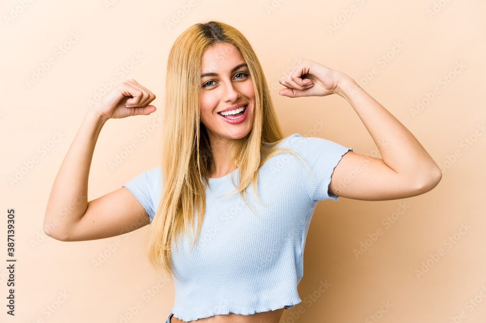 Young blonde caucasian woman showing strength gesture with arms, symbol of feminine power