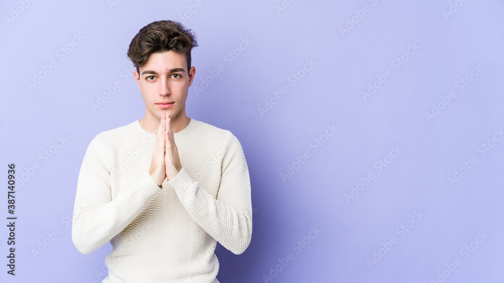 Young caucasian man isolated on purple background praying, showing devotion, religious person looking for divine inspiration.