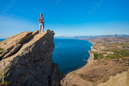 A young man stands on a picturesque rock ledge above the sea against the sky. The concept of travel and freedom. 