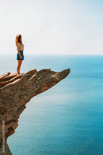 A young woman stands on a picturesque rock ledge above the sea against the sky. The concept of travel and freedom. 
