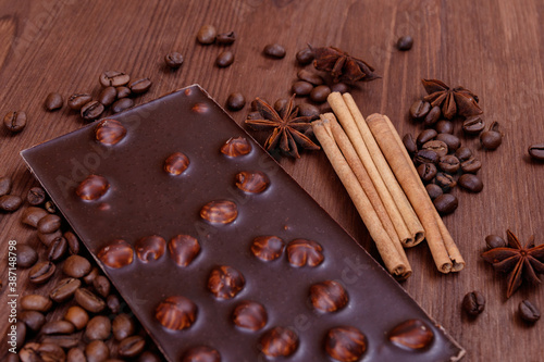 Chocolate bar with nuts on a wooden table with coffee beans and spices. Roasted coffee beans, cinnamon sticks and anise stars. Chocolate bar with hazelnuts. 