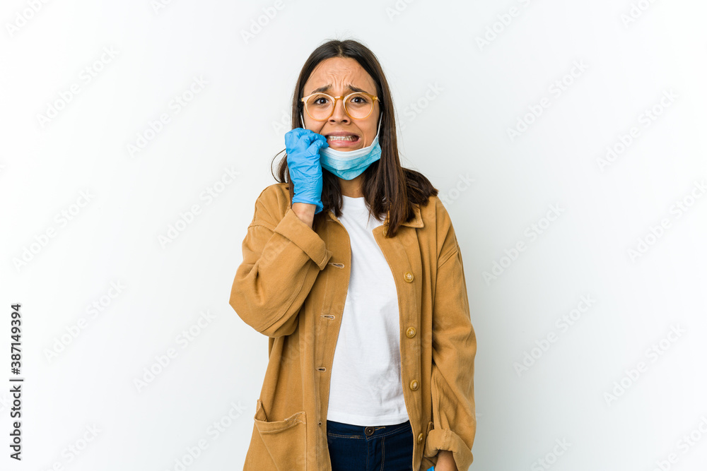 Young latin woman wearing a mask to protect from covid isolated on white background biting fingernails, nervous and very anxious.