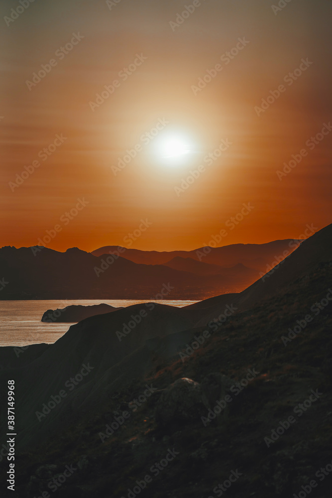 Hilly landscape by the sea in a bright orange sunset. Layers of mountains at sunset, background image