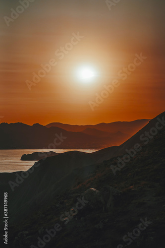 Hilly landscape by the sea in a bright orange sunset. Layers of mountains at sunset  background image