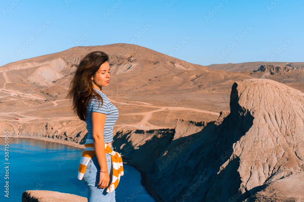 A young woman with long hair stands on the slope of Cape chameleon with an amazing panoramic view of the hills and the sea from above