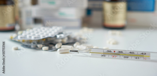 Bottle pills and medicine capsule on table, drugs and tablets boxes in background. Medical thermometer with a temperature of 38 degrees. Increased body temperature of a sick person. 