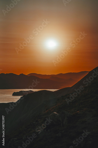 Hilly landscape by the sea in a bright orange sunset. Layers of mountains at sunset, background image