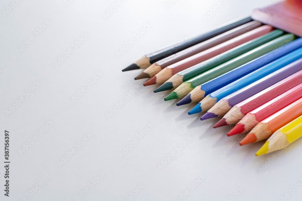 New multicolored pencils peeking out of a box, positioned on a white table with a signature area. Bright colors. Shadow from the slates. New multicolored pencils peeking out of a box, positioned on a white table with a signature area. Bright colors. Shadow from the slates.