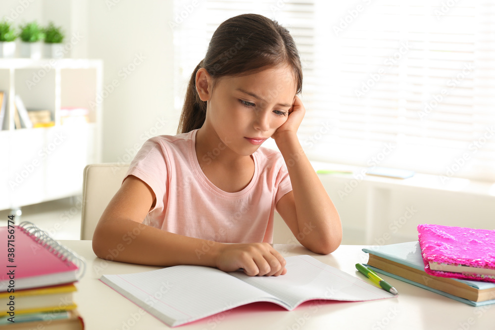 Sad little girl doing homework at table indoors Sad little girl doing homework at table indoors