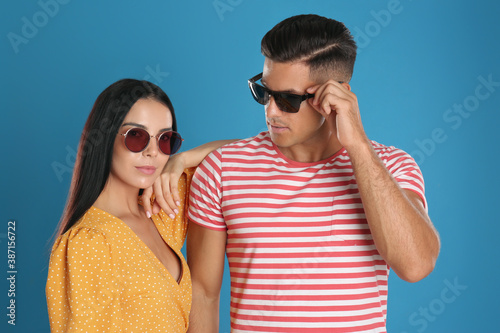Stylish couple wearing sunglasses on blue background