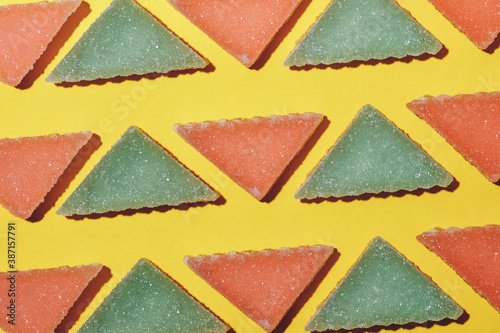 Pattern made of multicolored triangular jelly candy on yellow background. Macro shot.